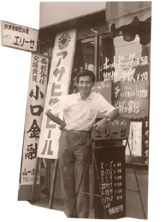 創業当初の店舗前に立つ人物